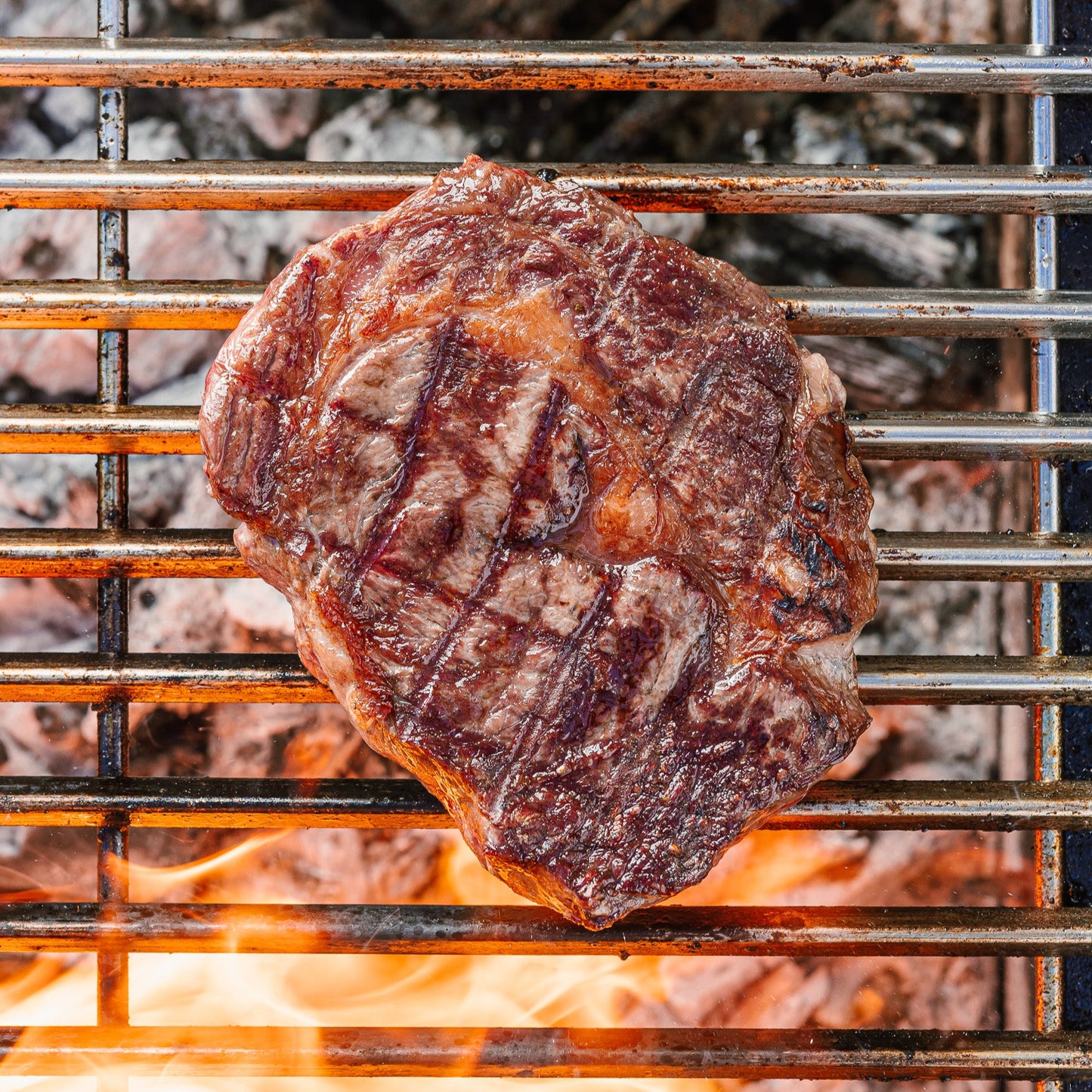 Grilled steak on a barbecue grill with flames below