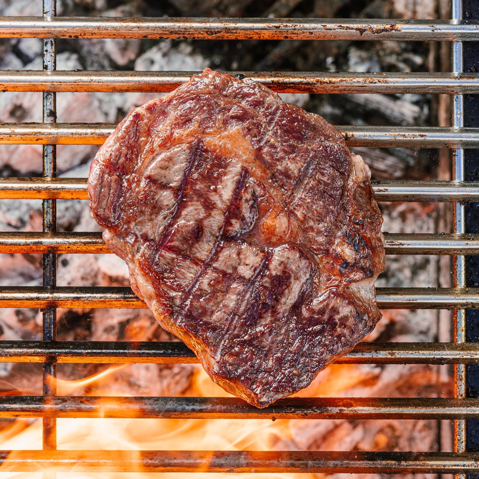 Grilled steak on a barbecue grill with flames below